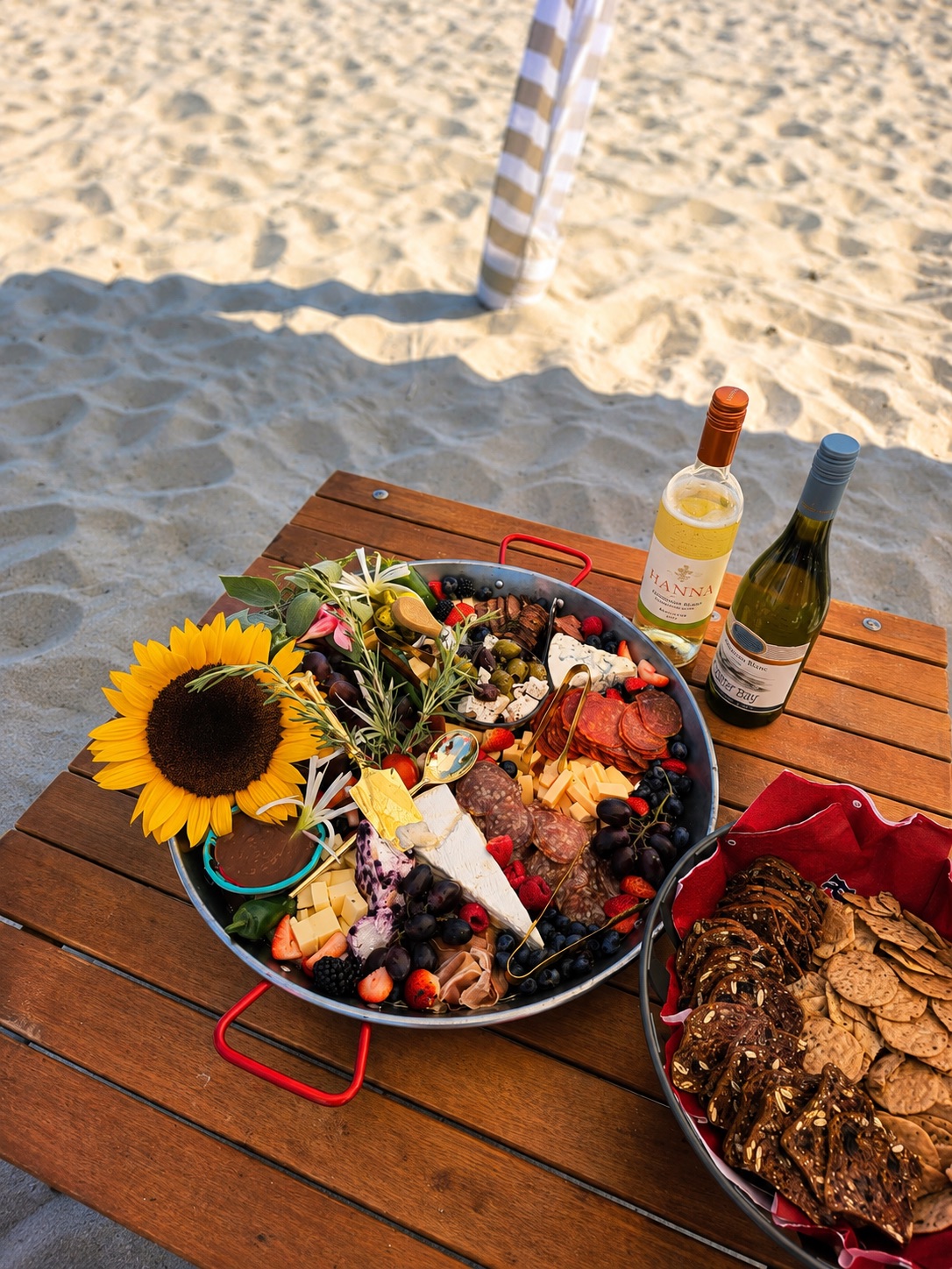 The real beach board: cheeses, cured meats, berries, and a sunflower arranged in a pan on a wooden table set in the sand